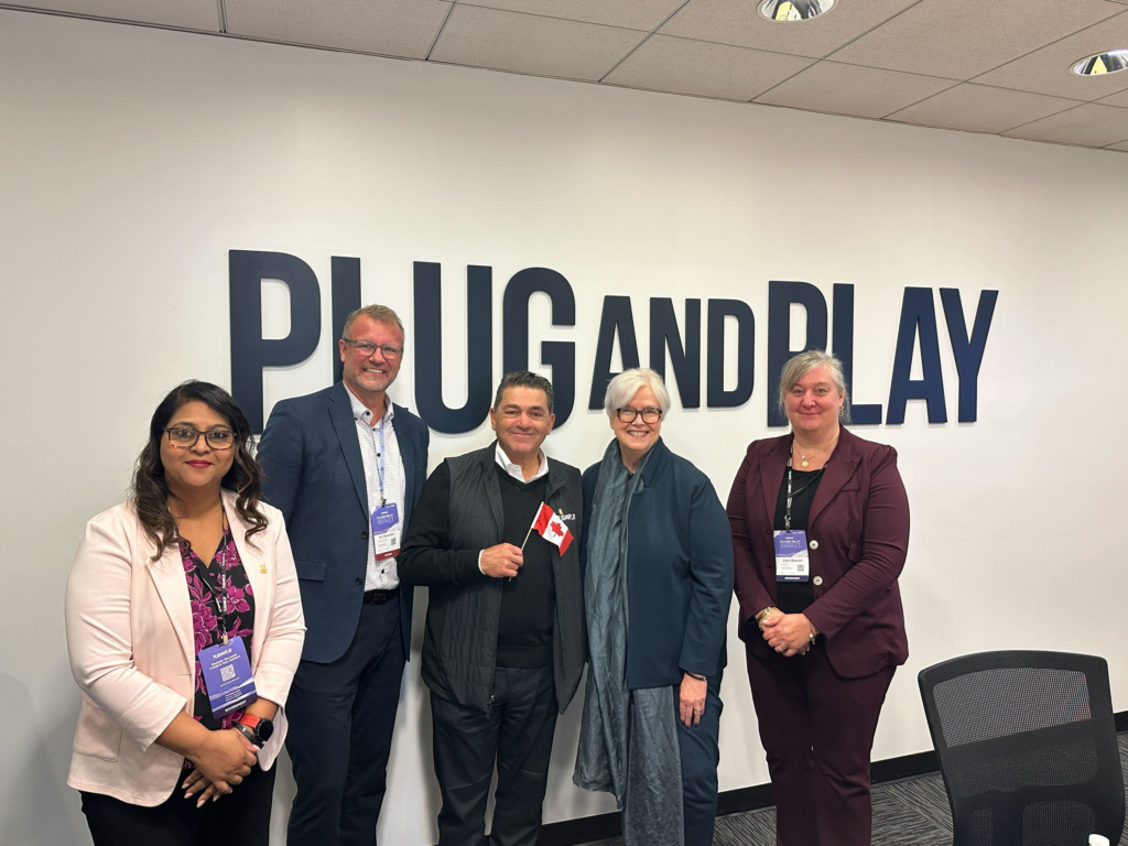 Representatives pose in front of the Plug and Play logo.