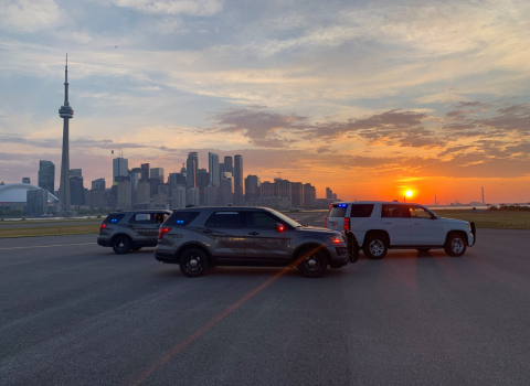 three security vehicles on the airport runway at sunrise with Toronto's skyline behind them