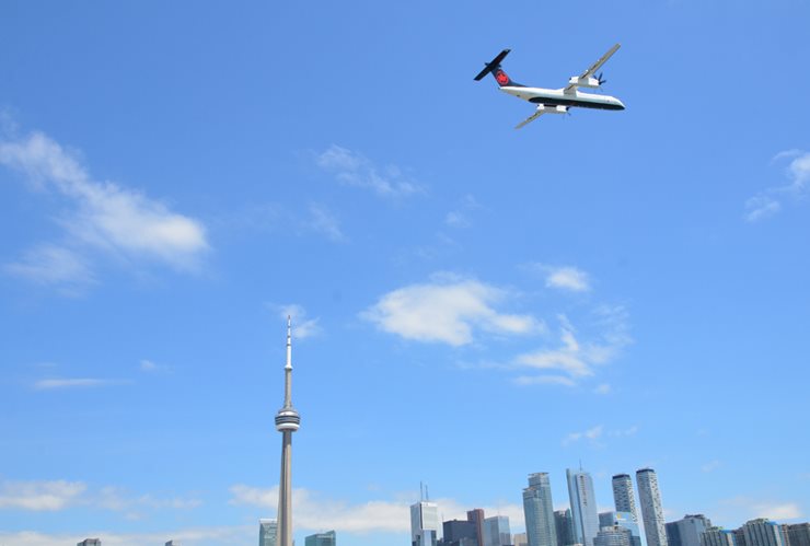 Photo taken from the ground of a plane in air with city in background