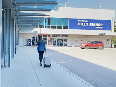 Passenger walks with suitcase to airport entrance.
