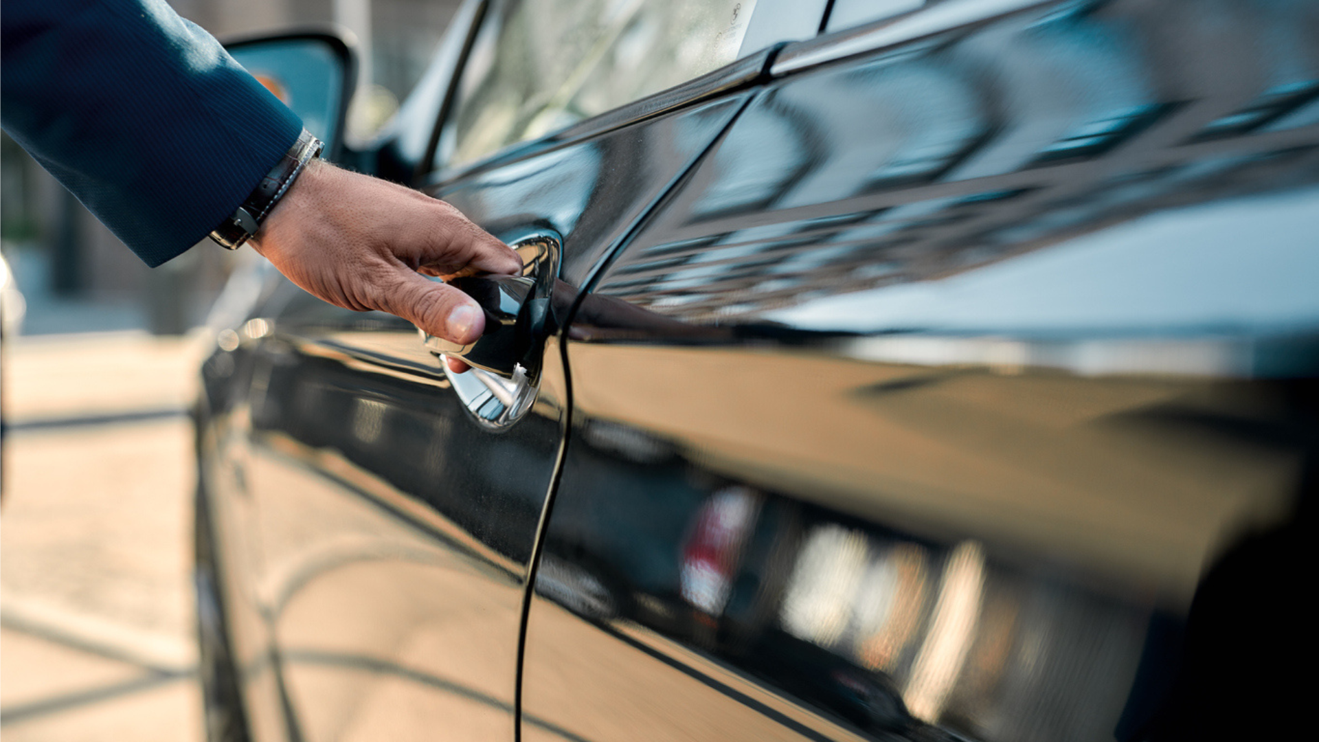 Male hand opening the door of a black car while standing outdoors