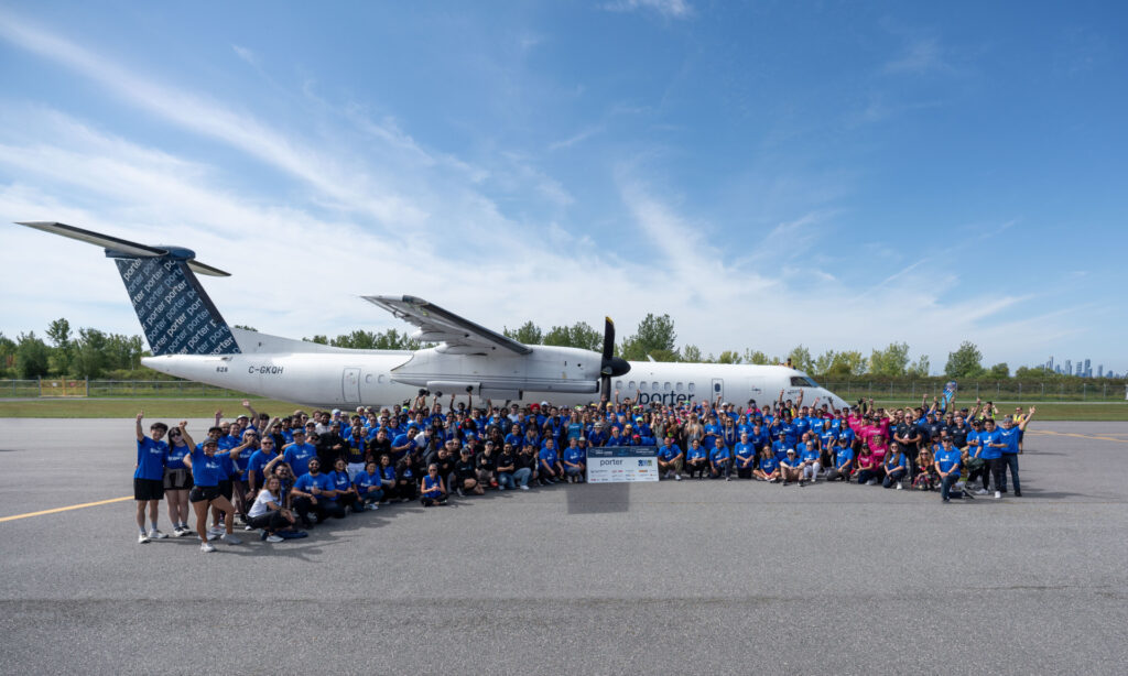 Large group of individuals posing for a photo in front of a Porter Airplane