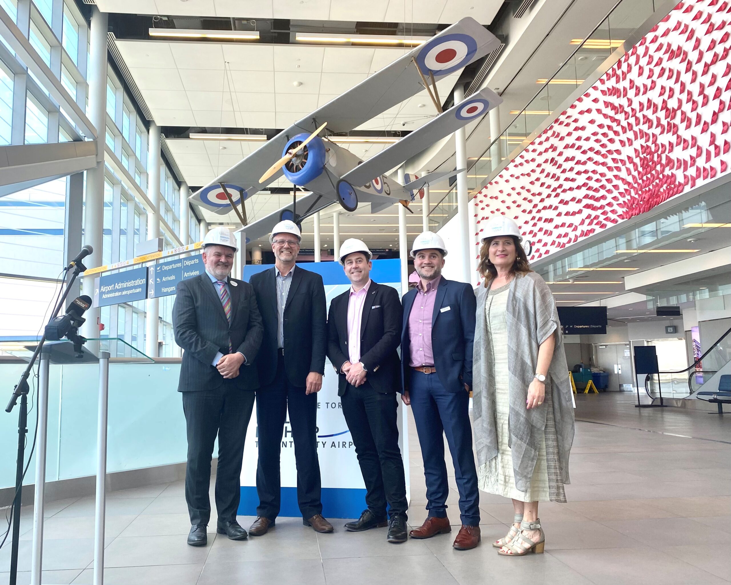 Representatives gather beneath the Nieuport model in the airport atrium.