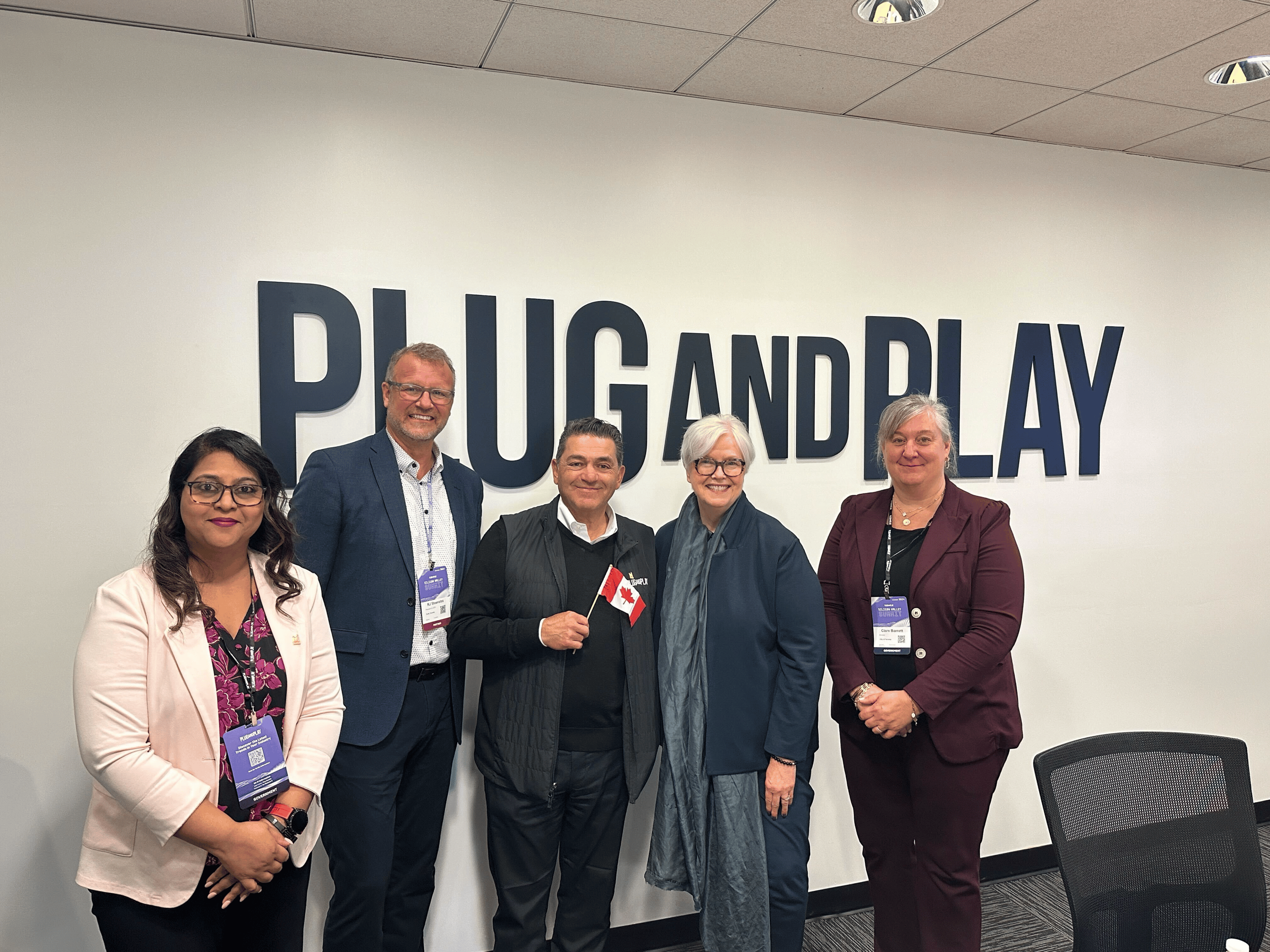 Representatives pose in front of the Plug and Play logo.