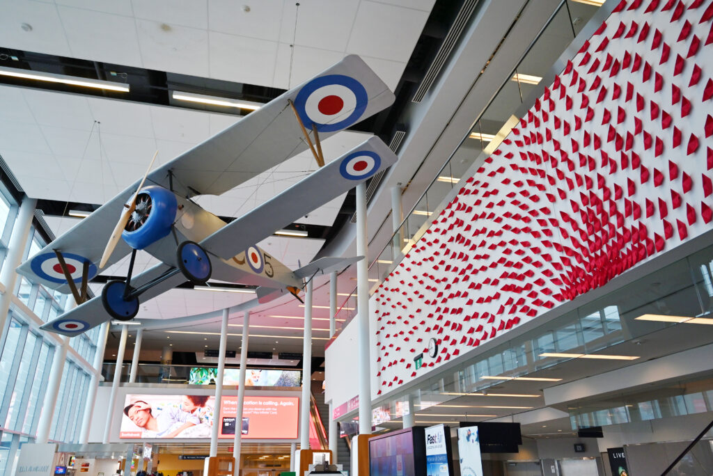 A Nieuport 17 model suspended in the airport atrium beside a red textile installation.
