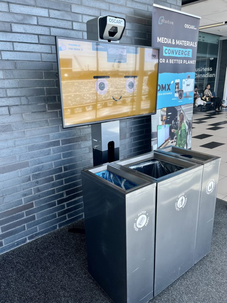 An Oscar Sort screen above waste and recycling bins at the airport.