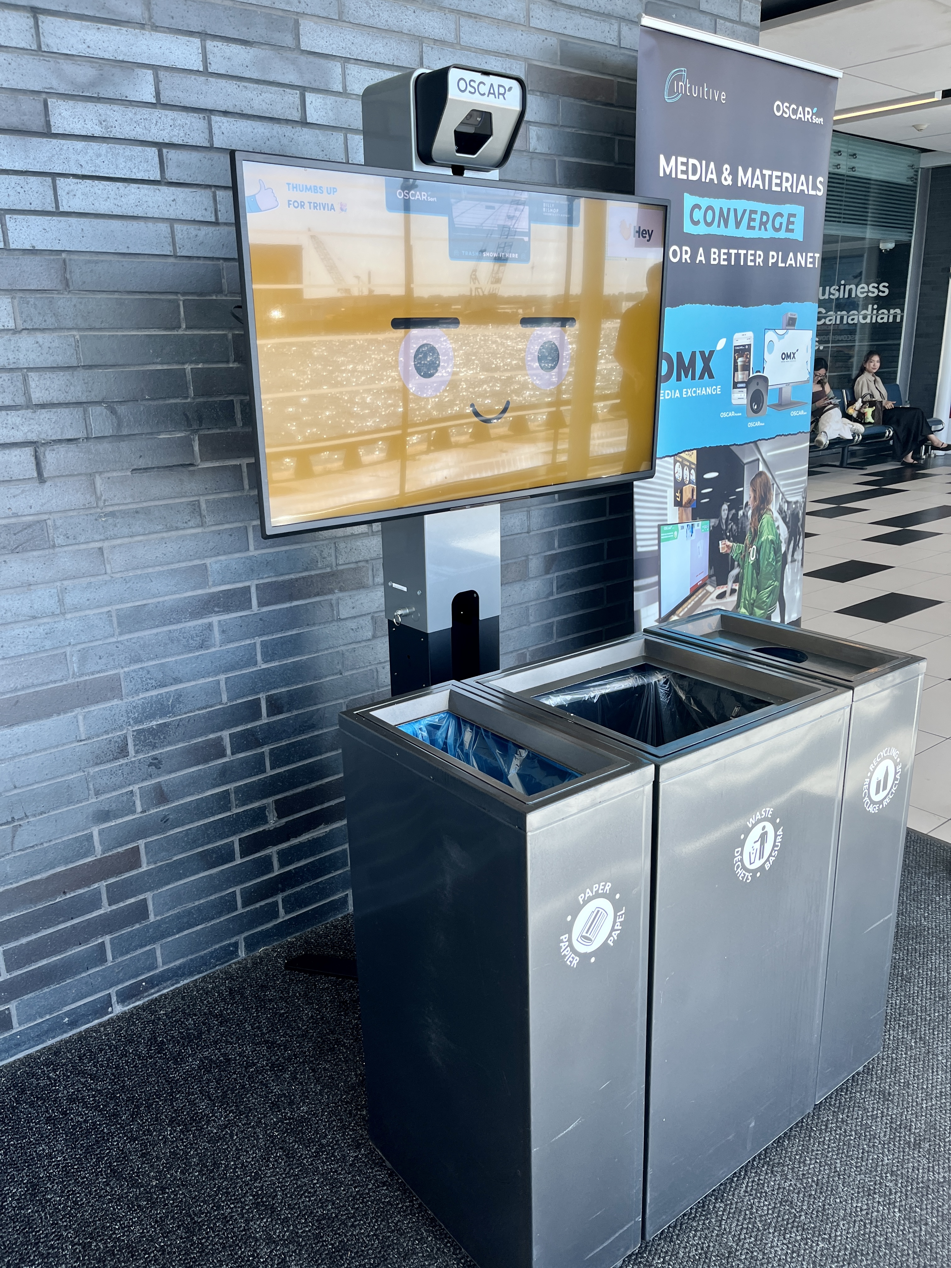 An Oscar Sort screen above waste and recycling bins at the airport.