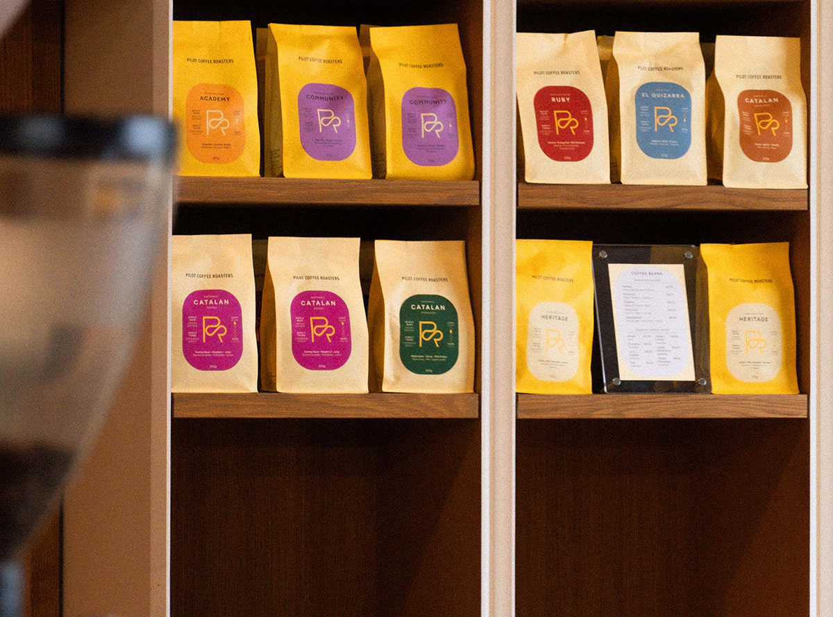 Bags of Pilot Coffee Roasters coffee displayed on wooden shelves.